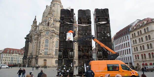 Drei senkrecht aufgestellte Busse vor einer Kirche, ein orangenes Auto mit Personenkran davor Drei senkrecht aufgestellte Busse vor einer Kirche, ein orangenes Auto mit Personenkran davor
