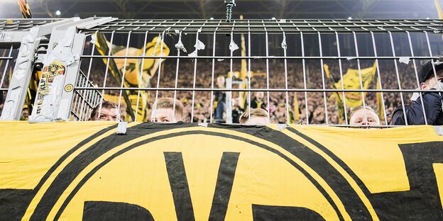 Eine BVB-Fahne am Tribünengitter, dahinter lugen ein paar Fangesichter hervor