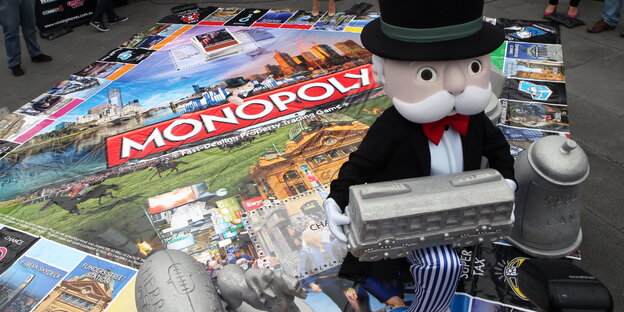 Ein Monopolymännchen sitzt auf einem großen Monopolybrett Ein Monopolymännchen sitzt auf einem großen Monopolybrett