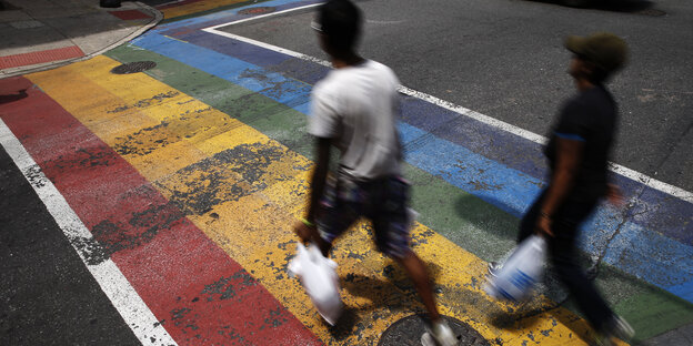 Zwei People of Colour laufen über einen rot-gelb-blau belamten Asphaltstreifen Zwei People of Colour laufen über einen rot-gelb-blau belamten Asphaltstreifen