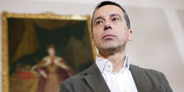 Ein Mann in Anzug und Hemd von unten fotografiert, im Hintergrund ein Gemälde Ein Mann in Anzug und Hemd von unten fotografiert, im Hintergrund ein Gemälde