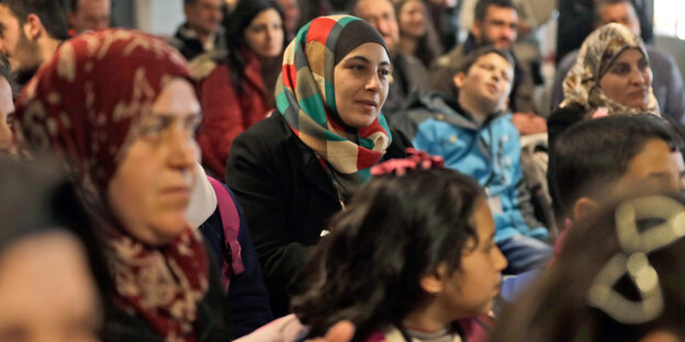 Viele Frauen mit Kopftüchern und Kinder sitzen zusammen und blicken in eine Richtung Viele Frauen mit Kopftüchern und Kinder sitzen zusammen und blicken in eine Richtung