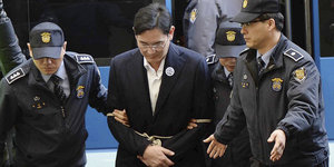 Zwei Polizisten begleiten einen Mann in Handschellen