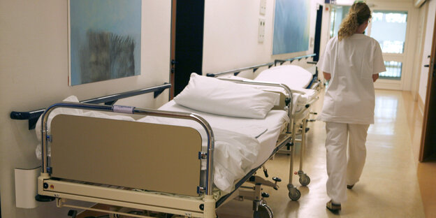 Eine Krankenschwester läuft in einem Flur an einem Krankenbett vorbei Eine Krankenschwester läuft in einem Flur an einem Krankenbett vorbei