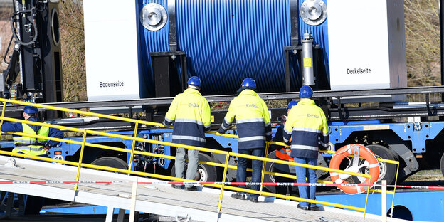Vier Männer mit Helmen schauen bei der Verladung von etwas großem zu Vier Männer mit Helmen schauen bei der Verladung von etwas großem zu