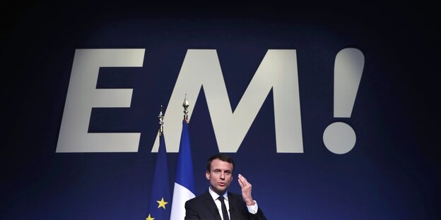 Macron auf einer Bühne vor seinen überdimensionierten Initialen „EM!“ Macron auf einer Bühne vor seinen überdimensionierten Initialen „EM!“