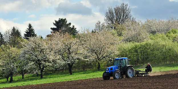 Ein Traktor fährt über ein Feld am Rande einer Streuobstwiese