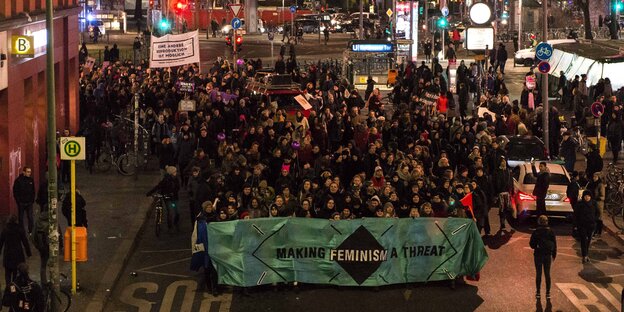 Eine Demonstrationszug, an dessen Spitze ein Transparent mit der Aufschrift „Making Feminism a Threat“ steht