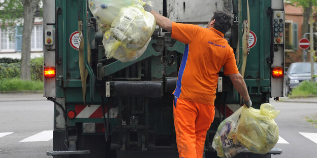 Ein Müllmann wirft zwei Plastiksäcke in den Müllabfuhrwagen Ein Müllmann wirft zwei Plastiksäcke in den Müllabfuhrwagen