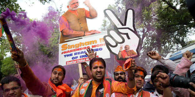 Mehrere Männer schwenken jubelnd Plakate von Indiens Premierminister Modi, sie sind in orange gekleidet Mehrere Männer schwenken jubelnd Plakate von Indiens Premierminister Modi, sie sind in orange gekleidet