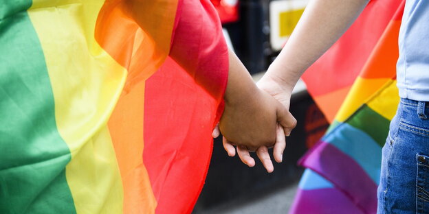 zwei Männer Hand in Hand, gehüllt in Regenbogenflaggen zwei Männer Hand in Hand, gehüllt in Regenbogenflaggen