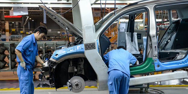 Zwei chinesische Arbeiter arbeiten in einer Fabrik an einem Auto Zwei chinesische Arbeiter arbeiten in einer Fabrik an einem Auto