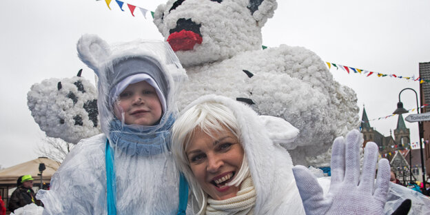 eine Mutter und ihr Kind im Eisbärkostüm vor einem riesigen Eisbären auf einem Karnevalswagen