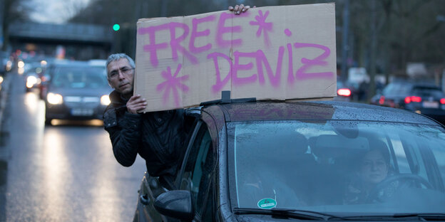 Ein Mann zeigt aus einem Auto heraus ein Schild mit der Aufschrift Free Deniz Ein Mann zeigt aus einem Auto heraus ein Schild mit der Aufschrift Free Deniz