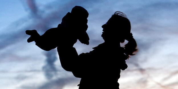 Eine Mutter hebt ihr Kind in die Luft vorm Abendhimmel Eine Mutter hebt ihr Kind in die Luft vorm Abendhimmel