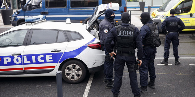 Männer in schwarzen Uniformen und Gesichtsmasken stehen am offenen Kofferraum eines Polizeiwagens Männer in schwarzen Uniformen und Gesichtsmasken stehen am offenen Kofferraum eines Polizeiwagens
