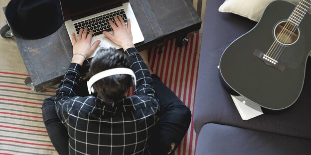 Ein junger Mann sitzt vor dem Laptop und neben ihm liegt eine Gitarre Ein junger Mann sitzt vor dem Laptop und neben ihm liegt eine Gitarre