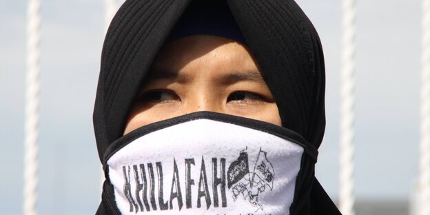 Verschleierte Frau mit Mundschutz, der die Aufschrift „Kalifat“ trägt Verschleierte Frau mit Mundschutz, der die Aufschrift „Kalifat“ trägt