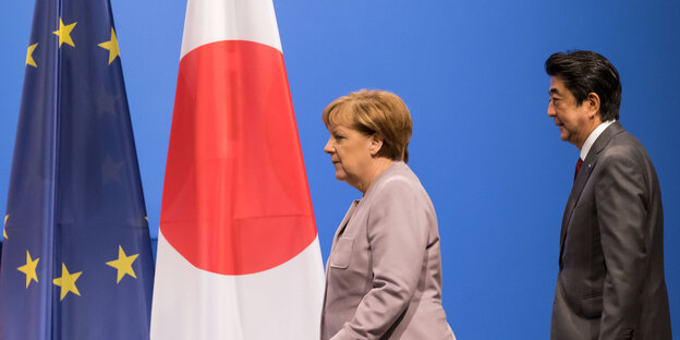 Angela Merkel und Shinzo Abe laufen in Richtung einer EU- und einer japanischen Fahne Angela Merkel und Shinzo Abe laufen in Richtung einer EU- und einer japanischen Fahne
