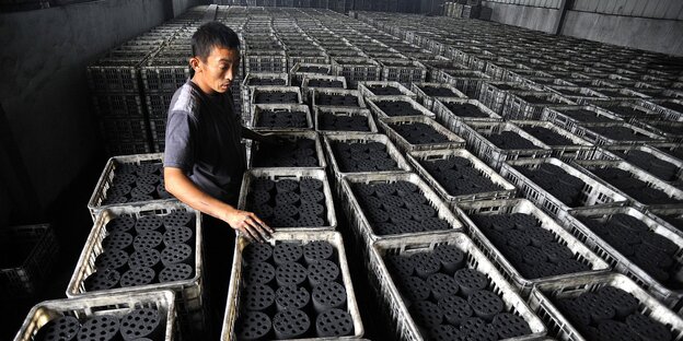 Ein chinesischer Arbeiter inmitten von Behältern mit Kohle Ein chinesischer Arbeiter inmitten von Behältern mit Kohle