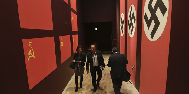 Zwischen Bannern mit Sowjet- und Hakenkreuzbannern gehen Besucher durch das Museum Zwischen Bannern mit Sowjet- und Hakenkreuzbannern gehen Besucher durch das Museum