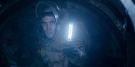 Ein Mann in Raumfahrt-Anzug hält einen Lichtstab vor sich und hat ein verängstigtes Gesicht