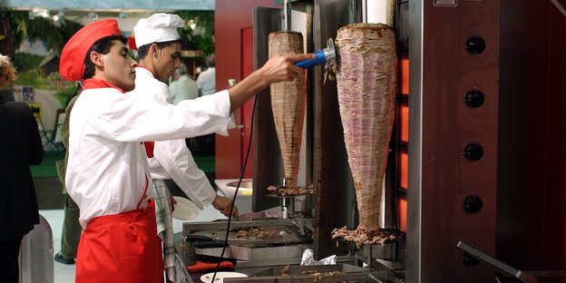 Ein Mann, der Dönerfleisch von einem Dönerspieß abschneidet Ein Mann, der Dönerfleisch von einem Dönerspieß abschneidet