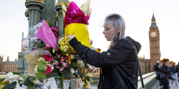 Eine junge Frau legt auf einer Straße vor dem Palace of Westminster Blumen ab Eine junge Frau legt auf einer Straße vor dem Palace of Westminster Blumen ab
