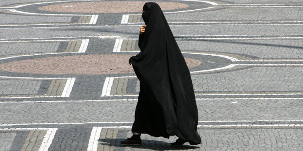 Eine ganz verschleierte Frau in schwarzer Burka läuft über einen Platz Eine ganz verschleierte Frau in schwarzer Burka läuft über einen Platz