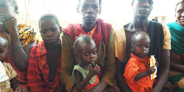 Drei Frauen mit ihren Kindern sitzen auf einer Bank vor dem Saint Mary's Hospital in einem Dorf im Südsudan und warten auf Hilfe. Drei Frauen mit ihren Kindern sitzen auf einer Bank vor dem Saint Mary's Hospital in einem Dorf im Südsudan und warten auf Hilfe.