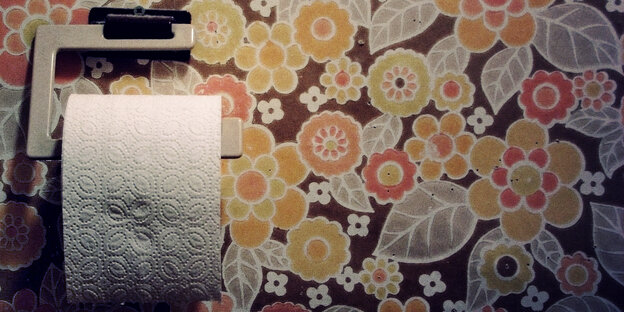 Vor einer alten Blümchentapete hängte eine Rolle Klopapier Vor einer alten Blümchentapete hängte eine Rolle Klopapier