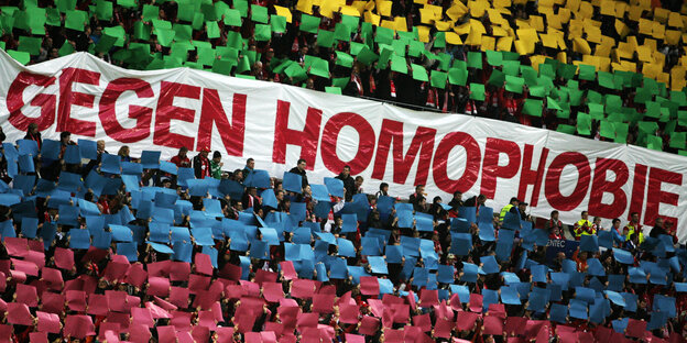 Ein großes Schild mit der Aufschrift "Gegen Homophobie", darüber und darunter halten Menschen Schilder in Regenbogenfarben hoch Ein großes Schild mit der Aufschrift "Gegen Homophobie", darüber und darunter halten Menschen Schilder in Regenbogenfarben hoch