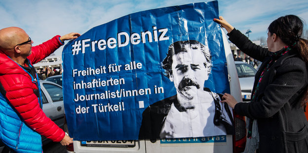 Zwei Menschen halten ein #FreeDeniz-Plakat hoch