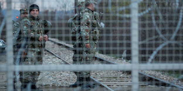Im Vordergrund Zaun mit Stacheldraht, im Hintergrund Soldaten Im Vordergrund Zaun mit Stacheldraht, im Hintergrund Soldaten
