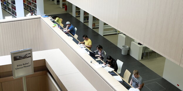 Menschen an einer längeren Reihe Arbeitsplätze in einer Bibliothek Menschen an einer längeren Reihe Arbeitsplätze in einer Bibliothek