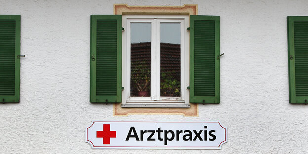 Ein geöffneter Fensterladen, daruntern ein Schild mit der Aufschrift „Arztpraxis“ Ein geöffneter Fensterladen, daruntern ein Schild mit der Aufschrift „Arztpraxis“