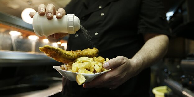 Koch streut Salz auf eine Portion Fish and Chips Koch streut Salz auf eine Portion Fish and Chips