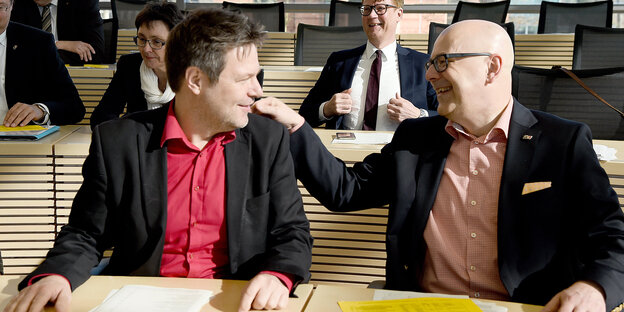 Robert Habeck und Torsten Albig sitzen an einem Tisch, Albig greift Habeck an die Schulter, beide lacen. Robert Habeck und Torsten Albig sitzen an einem Tisch, Albig greift Habeck an die Schulter, beide lacen.
