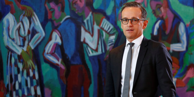Ein Mann in Anzug und mit Brille vor einer Graffit-besprühten Wand Ein Mann in Anzug und mit Brille vor einer Graffit-besprühten Wand