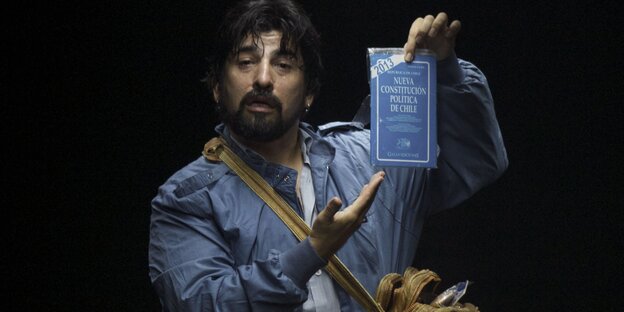 Ein Mann mit einer gelben Tasche hält ein blaues Buch in die Luft und zeigt darauf Ein Mann mit einer gelben Tasche hält ein blaues Buch in die Luft und zeigt darauf