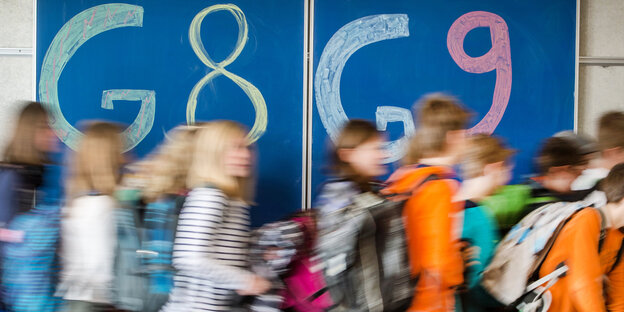 Schulkinder rennen vor einer Tafel, auf der links G8 und rechts G9 steht, nach rechts Schulkinder rennen vor einer Tafel, auf der links G8 und rechts G9 steht, nach rechts