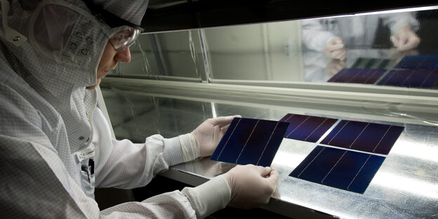 Ein Mann mit Schutzanzug betrachtet eine Solarzelle Ein Mann mit Schutzanzug betrachtet eine Solarzelle