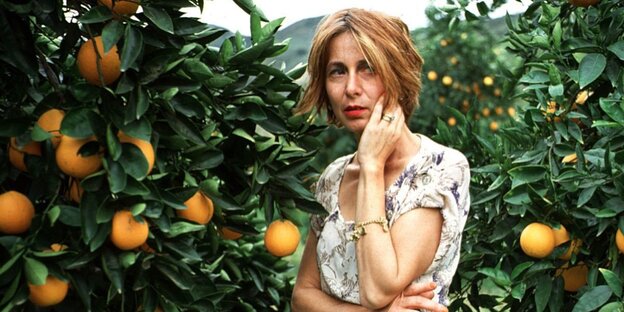 Chris Kraus steht, eine Hand an der Wange, in einem Garten zwischen Orangenbäumen Chris Kraus steht, eine Hand an der Wange, in einem Garten zwischen Orangenbäumen