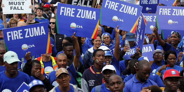 Menschen in blauen Shirts halten blaue Schilder hoch - Fire Zuma steht darauf Menschen in blauen Shirts halten blaue Schilder hoch - Fire Zuma steht darauf