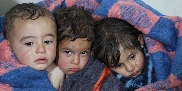 drei kleine Kinder, die, eng aneinandergeschmiegt, traurig in die Kamera blicken drei kleine Kinder, die, eng aneinandergeschmiegt, traurig in die Kamera blicken