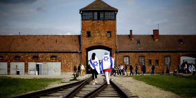 Zwei junge Leute mit Israel-Flaggen laufen über die Gleise zum Tor von Auschwitz-Birkenau Zwei junge Leute mit Israel-Flaggen laufen über die Gleise zum Tor von Auschwitz-Birkenau