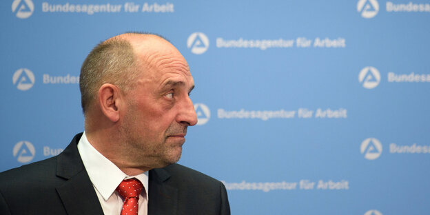 Ein Mann im Anzug vor einer Tapete der Bundesagentur für Arbeit Ein Mann im Anzug vor einer Tapete der Bundesagentur für Arbeit