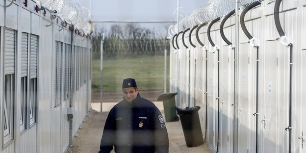 Ein Polizist hinter Stracheldraht steht zwischen zwei Wohncontainern