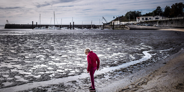 Eine Frau steht an einem Strand bei Ebbe Eine Frau steht an einem Strand bei Ebbe