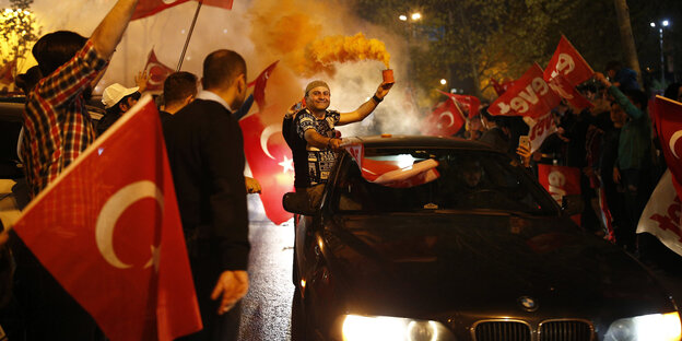 Menschen feiern auf der Straße. Sie schwenken türkische Fahnen und fahren im Autokorso Menschen feiern auf der Straße. Sie schwenken türkische Fahnen und fahren im Autokorso